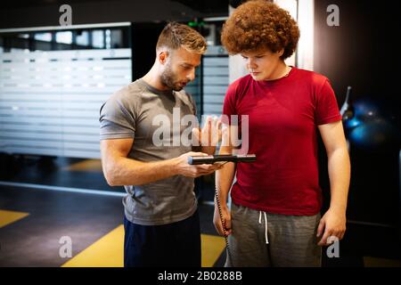 Fette junge Männer mit Trainer-Training im Fitness-Studio. Stockfoto