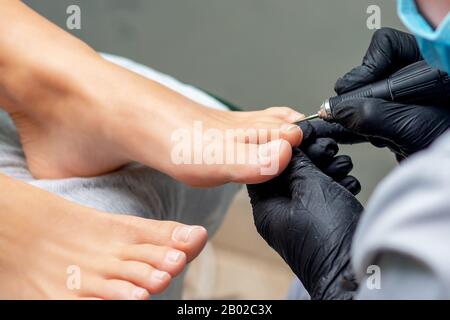 Pedicurist die Hände in Handschuhe mit Spezialwerkzeug, Pediküre der weiblichen Nägel auf die Füße. Fußpflege in Spa Salon, aus der Nähe. Stockfoto