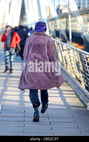 London, England, Großbritannien. Mann in einem violetten Kopftuch, Kopfhörer und Morgenmantel, der die Jublee Bridge überquert Stockfoto