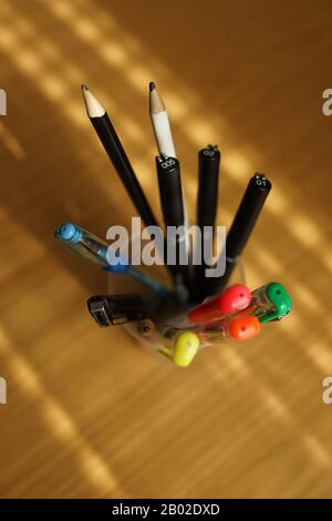 Bürobedarf auf einem Holztisch. Farbige Bleistifte und Kugelschreiber in einem Ständer. Stockfoto