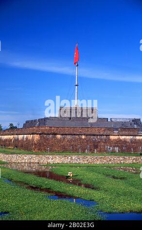 Vietnam: Ein kleines Boot navigiert den Graben vor dem Flaggenturm der Kaiserstadt, der Zitadelle, Hue, um 1995. Kaiser Gia Long ordnete 1805 den Bau der Zitadelle von Hue an. Der weitläufige Komplex wurde nach den Vorstellungen des Fengshui oder der chinesischen Geomanz errichtet, aber nach den militärischen Prinzipien des bekannten französischen Militärarchitekten Sebastien de Vauban aus dem 18. Jahrhundert. Das Ergebnis ist eine ungewöhnliche und elegante Hybride, eine kaiserliche Stadt im chinesischen Stil, die sorgfältig mit den umliegenden Hügeln, Inseln und Wasserstraßen ausgerichtet ist, aber von massiven Ziegelmauern zwischen 6-12 Metern und 2,5 Metern Dicke geschützt wird Stockfoto