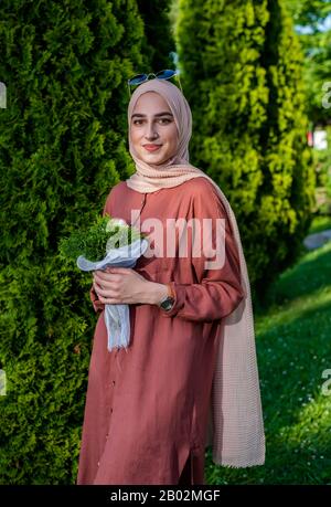 Junge Frau im Hijab, die Blumen in islamischer Kleidung hält Stockfoto