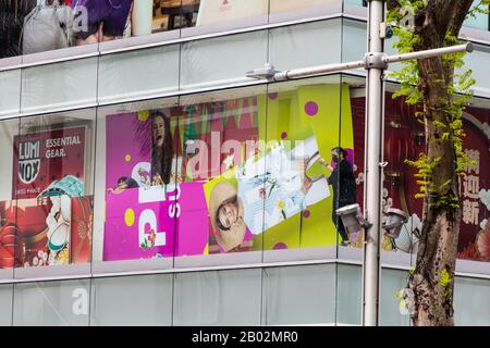 Die Mitarbeiter des Einzelhandels ändern die Anzeigetafel/Platine auf dem Fensterdisplay. Orchard Road, Singapur. Stockfoto