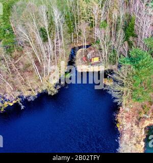 Luftbild von der Spitze eines dunkelblauen Moorseens in der Heide mit einer kleinen Hütte am Ufer Stockfoto