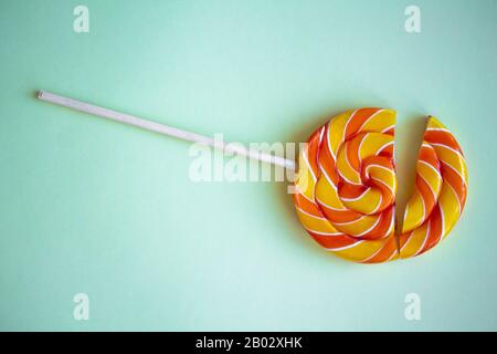 Kaputter Drall-Lollipop auf mintgrünem Hintergrund. Zwei Hälften bunter verdrehter Süßigkeiten. Nahaufnahme des Regenbogens rund süß auf Stock. Konzept des enttäuschend Stockfoto