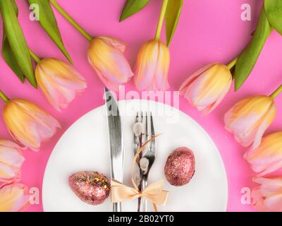 Schöne luxuriöse easter Tischbestecke wie Messer, Gabel mit bunten Tulpen und goldbemalten Eiern mit Glitzern auf rosa Oberfläche. Weihnachtshintergrund, Grußkarte, Nahaufnahme Stockfoto