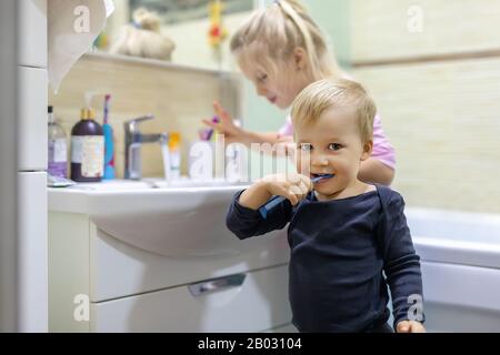 Zwei süße, hübsche blonde, kaukasische Geschwister, die morgens im Bad das Gesicht waschen und den Zahn mit Zahnbürste reinigen. Kleine Kinder Bruder und Stockfoto