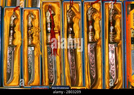 Die kleine von Uiguren dominierte Oase Yengisar (Yingjisha) ist in der gesamten westchinesischen Provinz Xinjiang für die Herstellung von handgefertigten Messern bekannt. Die Kleine Messerfabrik (Pichak Chilik Karakhana/Xiadaochang) beschäftigt erfahrene Handwerker vor Ort, die feine Messer mit eingelegten Griffen herstellen. Fast jeder uigurische Mann trägt ein Messer, sowohl als Zeichen der Manschaft als auch für den utilitareren Zweck, Melonen aufzuschneiden, und die wertvollsten (und teuersten) stammen aus Yengisar. Stockfoto