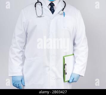 Arzt in einem weißen Mantel, blaue Latexhandschuhe, ein Stethoskop, das an seinem Hals hängt, Arzt mit einem grünen Papierhalter mit einem weißen leeren Blatt Stockfoto
