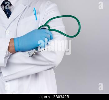 Ein ausgewachsener männlicher Arzt in einem weißen medizinischen Mantel steht und hält ein grünes Stethoskop auf weißem Hintergrund, einen Kopierraum Stockfoto