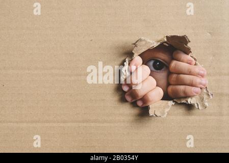 Kleines Mädchen, das aus einem Loch auf dem Pappkarton schält. Konzept des Menschenhandels, Der Spionage und Der Neugier Stockfoto