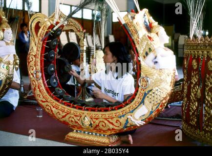 Thailand: Eine junge Frau spielt das khong MON, ein gong-Kreisinstrument, in einem traditionellen thailändischen Orchester in Bangkok. Die khong MON ist ein gong-Kreis-Instrument, das mit den Mon-Menschen auf dem südostasiatischen Festland in Verbindung gebracht wird. Er produziert die gleiche Tonhöhe wie der eher verbreitete khong wong gong Kreis, aber anstatt auf dem Boden zu ruhen, erstreckt sich der Holzrahmen des khong MON in Form eines Hufeisens in die Luft. Das Bild einer halb-Mann-halb-Vogel-Figur, die auf den Rahmen geschnitzt ist, ist traditionell und soll einen himmlischen Musiker symbolisieren. Stockfoto