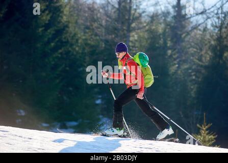 Mann allein mit Ski auf dem Berg. Kerl mit Rucksack auf einem verschwommenen Waldhintergrund am sonnigen Tag. Ski-Saison und Wintersportkonzept Stockfoto