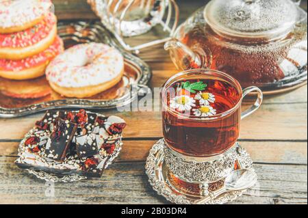 Kamillentee in einem Glasglas mit Schokolade und Donuts in Vereisung. Stockfoto