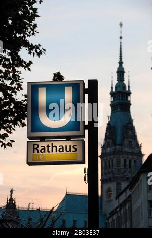 Ein aufgeleuchtes U-Bahn-Schild in der Nähe des Hamburger Rathauses mit dem Turm in Hamburg Stockfoto