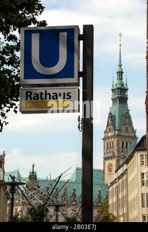 Ein aufgeleuchtes U-Bahn-Schild in der Nähe des Hamburger Rathauses mit dem Turm in Hamburg Stockfoto