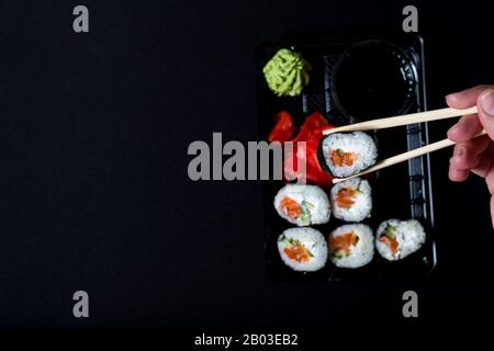 Sushi-Service. Set Sushi in Kunststoffbox auf schwarzem Hintergrund. Auswahl der Rolle aus Box mit Sushi. Stockfoto