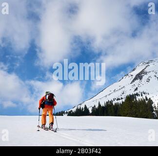 Rückblick auf Skifahrer Tourist Rucksacktourist in heller Kleidung Wandern auf Skiern bergauf vor blauem Himmel und schöner Bergwelt. Winterurlaub, aktives Lifestyle-, Ski- und Erholungskonzept. Stockfoto