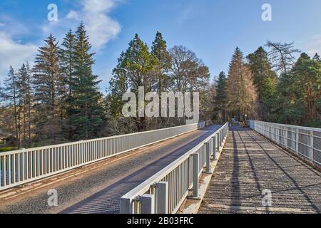 CARRON VILLAGE MORAY SCOTLAND DIE EINZIGARTIGE CARRON ROAD UND DIE ALTE EISENBAHNBRÜCKE, DIE DEN FLUSS SPEY ÜBERQUERT Stockfoto