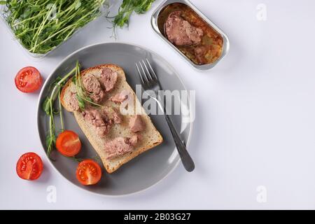 Gesunde Lebensmittel, Sandwich mit Dorschleber, Erbsenmikrogrin und Kirschtomaten auf einer grauen Platte auf weißem Grund Stockfoto