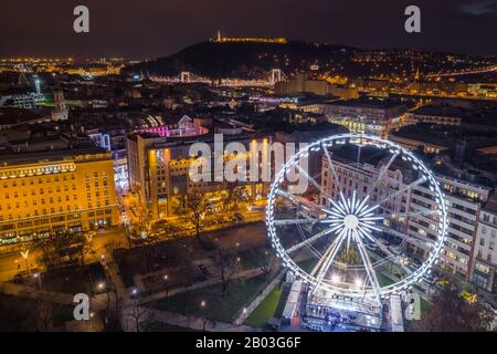 Budapest, Ungarn - Beleuchtetes Riesenrad am Elisabeth-Platz im Zentrum von Budapest mit Freiheitsstatue, Elisabeth-Brücke und anderem berühmten l Stockfoto