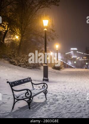 Budapest, Ungarn - Bank- und Lampenpfosten in einem verschneiten Park im Buda-Viertel mit Szechenyi-Kettenbrücke im Hintergrund während der schweren Schneeschuhzeit im Winter Stockfoto