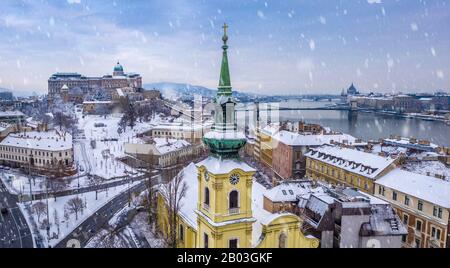 Budapest, Ungarn - katholische Kirche mit schneebedecktem Buda-Viertel, Königspalast der Burg Buda, Varkert Basar, Szechenyi-Kettenbrücke und Parlament am Rücken Stockfoto