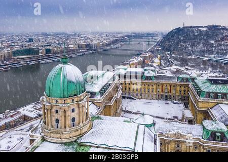 Budapest, Ungarn - Blick Auf Das verschneite Königspalast von Buda mit Freiheitsstatue, Elisabeth- und Freiheitsbrücke und Gellert Hill im Winter Stockfoto