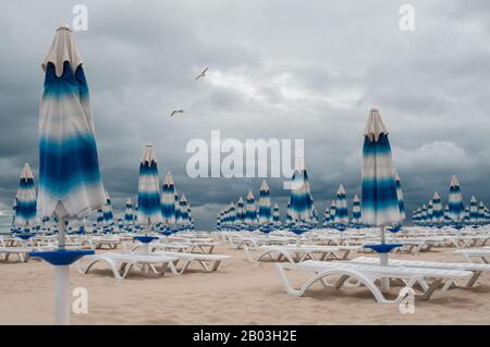 Geschlossene Sonnenschirme am Meer vor grauem Himmel. Stockfoto