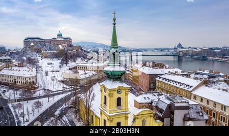 Budapest, Ungarn - katholische Kirche mit schneebedecktem Buda-Viertel, Königspalast der Burg Buda, Varkert Basar, Szechenyi-Kettenbrücke und Parlament am Rücken Stockfoto