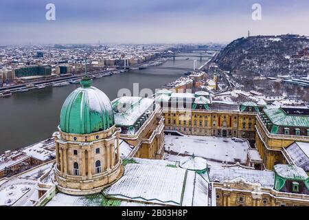 Budapest, Ungarn - Blick Auf Das verschneite Königspalast von Buda mit Freiheitsstatue, Elisabeth- und Freiheitsbrücke und Gellert Hill im Winter Stockfoto