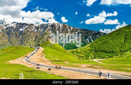 Touristen, die in Richtung Gergeti Trinity Church unter dem Berg Kazbegi in Georgia laufen Stockfoto