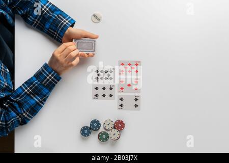 Eine Draufsicht über den Händler, der Chips und Karten im Pokerspiel auf weißem Tisch hält Stockfoto