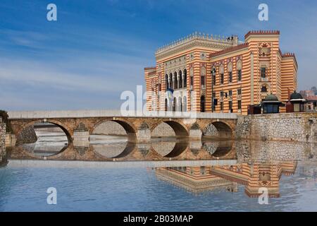 Reflexionen der alten Bogenbrücke mit nationalem und universitären Bibliotheksgebäude, einst Rathaus, Sarajevo, Bosnien und Herzegowina Stockfoto