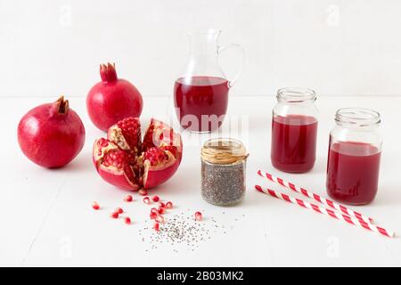 Pitcher und zwei Gläser frischen Granatapfelsaft, mit drei reifen Granatäpfeln, einer frisch geschält. Rouge Granatapfelsamen und chia Samen im Vorland Stockfoto