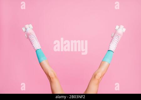 3/4-Blick auf hübsche, attraktive lange, schlanke Beine mit blauen, bequemen Socken Skatewalzen, die sich über rosafarbenem Pastell isoliert haben Stockfoto