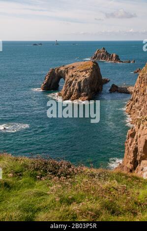 Blick über die Keltische See von Land's End, Cornwall, über die dramatische Landschaft mit Enys Dodnan Arch und Longshuses Lighthouse in der Ferne. Stockfoto