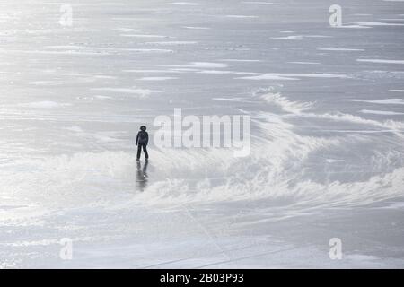 Frau, die an einem windigen Tag mit einem Schneesturm auf dem gefrorenen Eis des Baikalsee spaziert. Baikalsee, Sibirien, Russland. Stockfoto