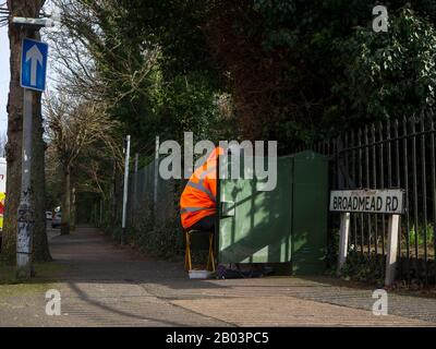 Telekommunikationsingenieur, der an einer grünen Schrankbox in einem Wohngebiet arbeitet Einbahnstraße Stockfoto