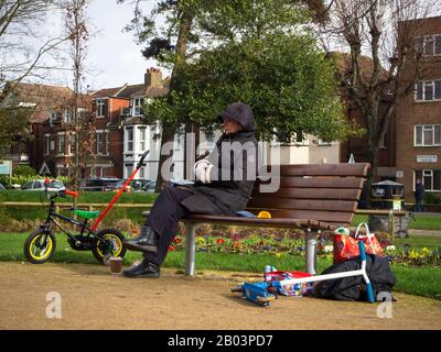 Frau, die auf einer Parkbank sitzt und auf Kinder wartet, während sie spielen Stockfoto