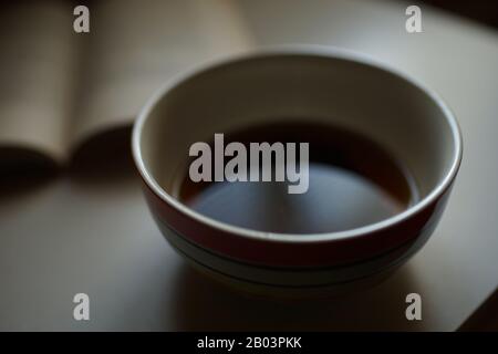 Teetasse und offenes Buch auf dem Tisch. Seitenansicht. Stockfoto