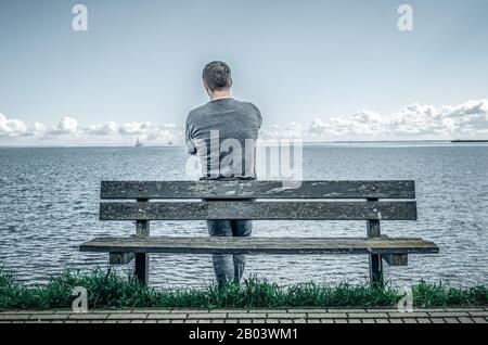 Ein Mann steht an einer Bank am Meer. Stockfoto