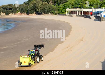 Whitmore Bay Beach bei Barry Island, Wales, früh an einem hellen, sonnigen Sommermorgen der Wurf durch einen roten Traktor ziehen einer Friseur Surfen Rechen gesäubert werden. Stockfoto