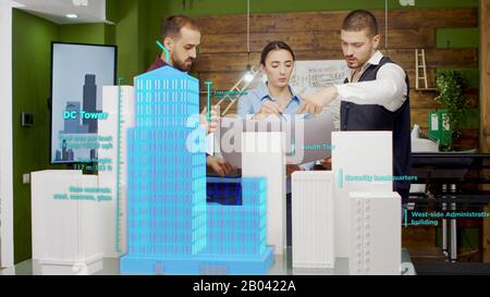 Team von Architekten, die an Wolkenkratzern in der Stadt arbeiten und dabei Hologramme für erweiterte Realität verwenden. Hologramme, die 3D-Gebäudemodelle abdecken Stockfoto