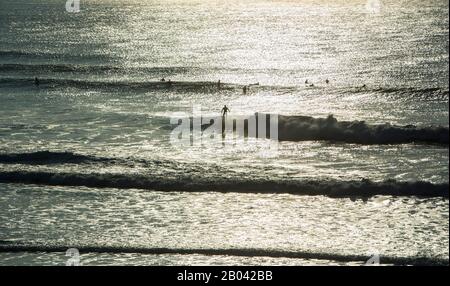 Ein Surfer reitet eine Welle, während andere Surfer warten, Fistral Beach, Newquay, Die Küste von Cornwall, England Stockfoto