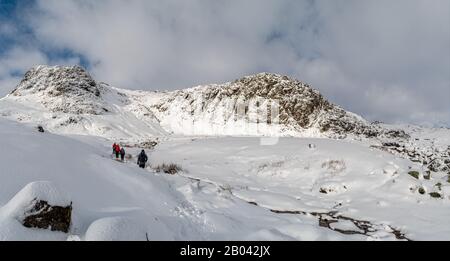 Wanderer, die sich im Stickle Tarn von der Spitze von Stickle Ghyll im Neuschnee dem Staudamm nähern Stockfoto