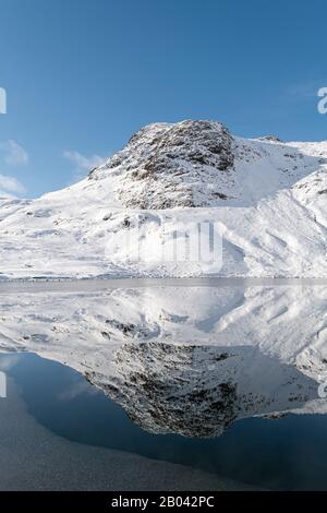 Ein majestätischer schneebedeckter Harrison Stickle spiegelte sich perfekt in einem teilweise gefrorenen Stickle Tarn wider Stockfoto