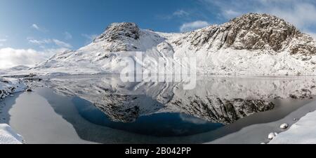 Die schneebedeckten Harrison Stickle und Pavey Arc spiegelten sich in einem teilweise gefrorenen Stickle Tarn wider Stockfoto