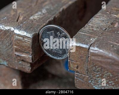 Einen russischen Rubel auf beiden Seiten mit einem Metall-Schraubstock einspannen. Konzept finanzieller und geschäftlicher Probleme. Die Wirtschaft ist im Griff Stockfoto