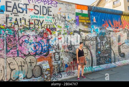 Junge Frau posiert vor Wandbild an der Ostseitengalerie Stockfoto